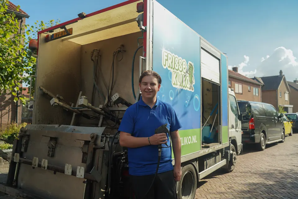 Medewerker in een blauwe Frisse Kliko-polo naast de bestickerde reinigingswagen.